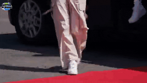 a person walking on a red carpet with a car in the background that says g ' clock