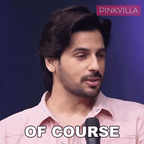 a man in a pink shirt is speaking into a microphone and the words of course are visible