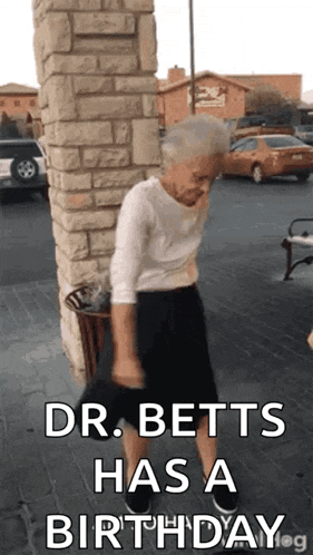 an elderly woman is standing in front of a brick wall and dancing .