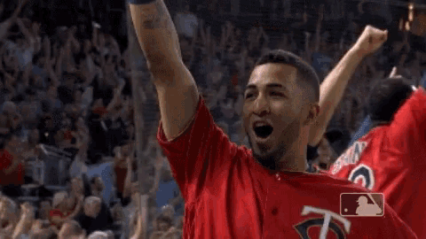 a baseball player in a red jersey is raising his arms in the air in front of a crowd .