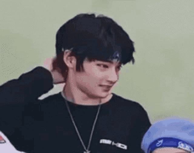 a young man wearing a black shirt and a blue headband is smiling and holding his hair .