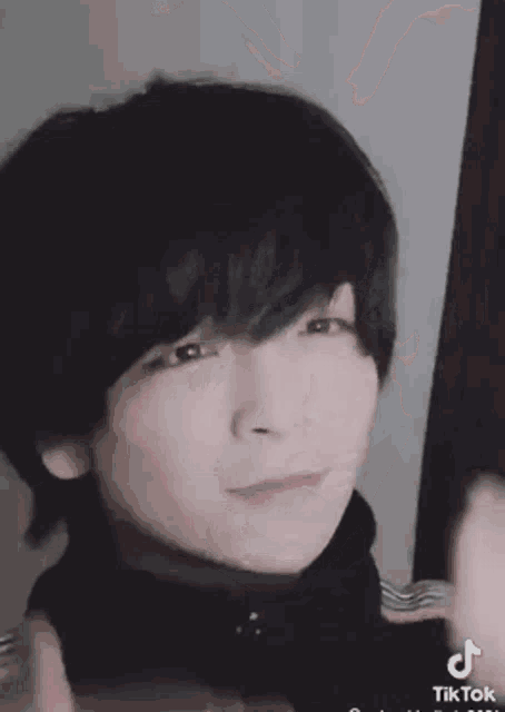 a close up of a person 's face with short black hair and a black turtleneck .