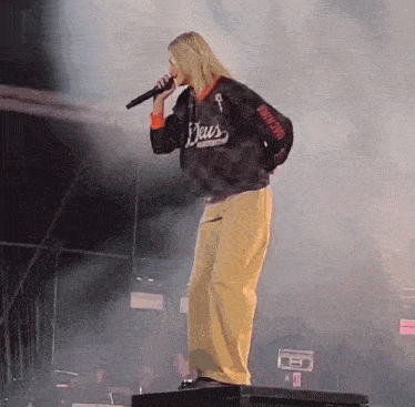 a woman singing into a microphone while wearing a sweatshirt that says deus