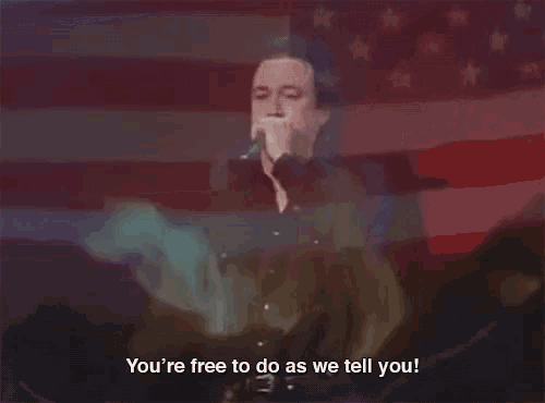 a man singing into a microphone with the words " you 're free to do as we tell you " next to him