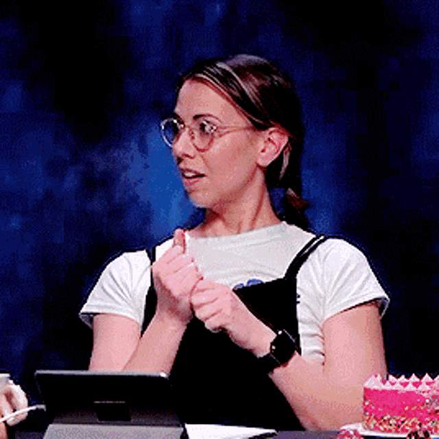 a woman wearing glasses is sitting at a table with a cake in front of her
