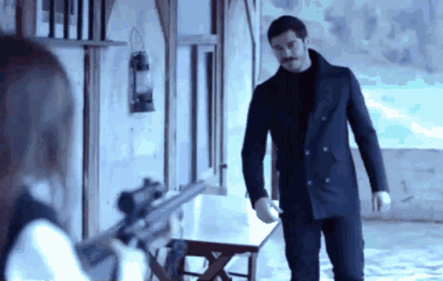 a man in a black coat stands next to a woman holding a rifle