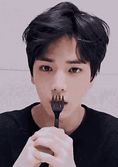 a young man is holding a fork in his mouth and eating something .