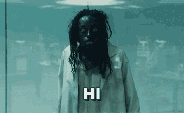 a man with black hair and dreadlocks is wearing a lab coat and a mask and saying hi .