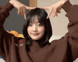 a woman wearing a brown sweater with a red bow on it is making a heart with her hands
