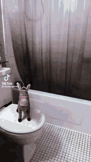 a stuffed donkey sitting on a toilet next to a bathtub