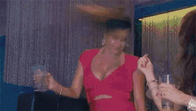 a woman in a pink dress is holding a glass of wine and dancing in a club .