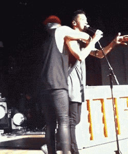 a man holding another man 's arm while singing into a microphone on stage