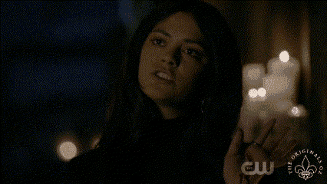 a woman in a dark room with candles in the background and a logo for cw