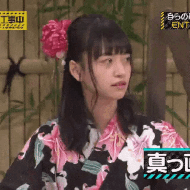 a girl in a kimono with a flower in her hair is looking at the camera .