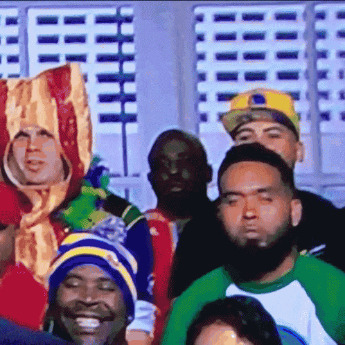 a group of people sitting in a stadium with one man wearing a bacon hat