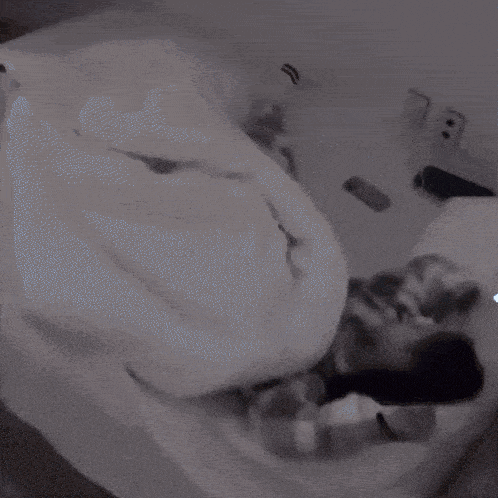 a person laying on a bed with a blanket and a cell phone