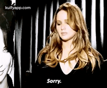 a woman is standing in front of a black and white curtain and says `` sorry '' .