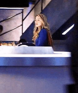 a woman in a blue shirt is sitting at a counter with stairs in the background .