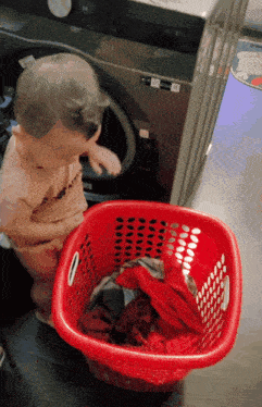a baby stands next to a red laundry basket full of clothes