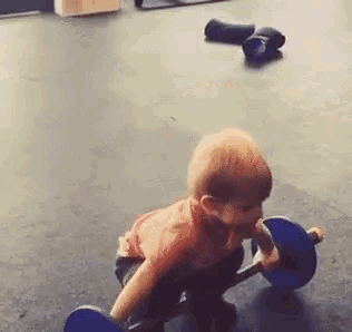 a young boy is lifting a barbell on the floor in a gym .