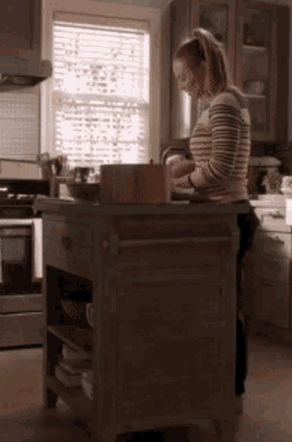 a woman in a striped sweater is standing in a kitchen