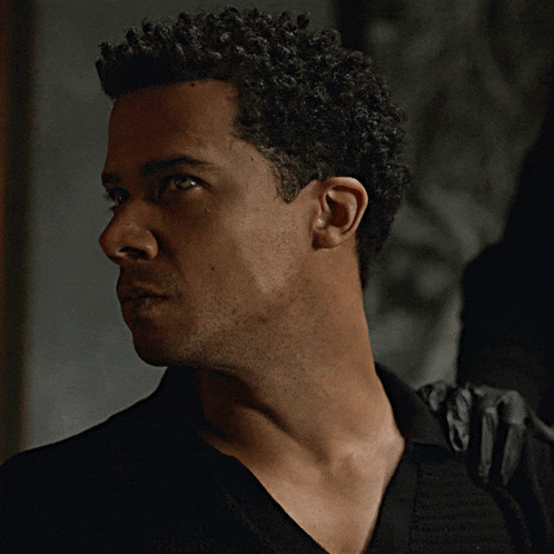 a man with curly hair and a black shirt looks at the camera