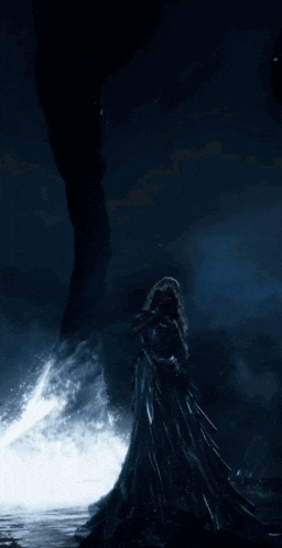 a woman in a long black dress is standing in front of a tornado in the dark