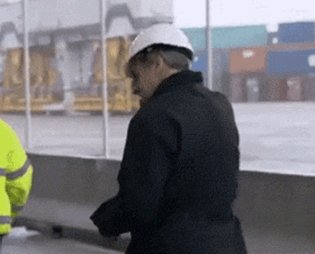a man wearing a hard hat stands next to another man in a yellow vest