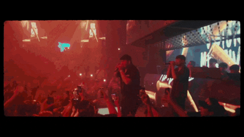 a man singing into a microphone in front of a crowd that is holding up their phones