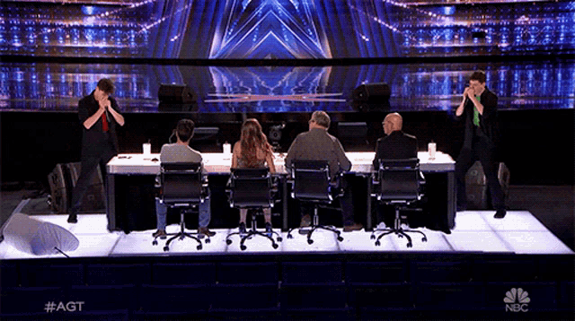a group of people sitting in chairs on a stage with a nbc logo in the background