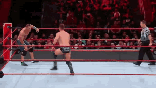 two men are wrestling in a wrestling ring with a referee in the background .