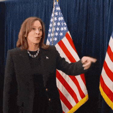 a woman is standing in front of an american flag and pointing
