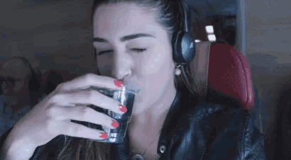 a woman wearing headphones is drinking from a glass while sitting on an airplane .