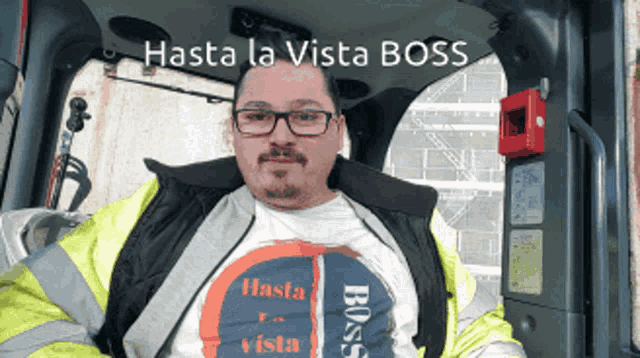 a man wearing a shirt that says hasta la vista boss is sitting in a vehicle
