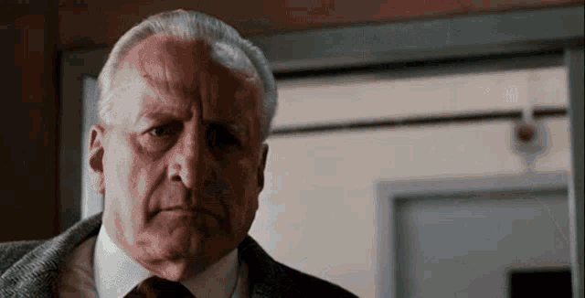 an older man in a suit and tie looks at the camera with a serious look on his face