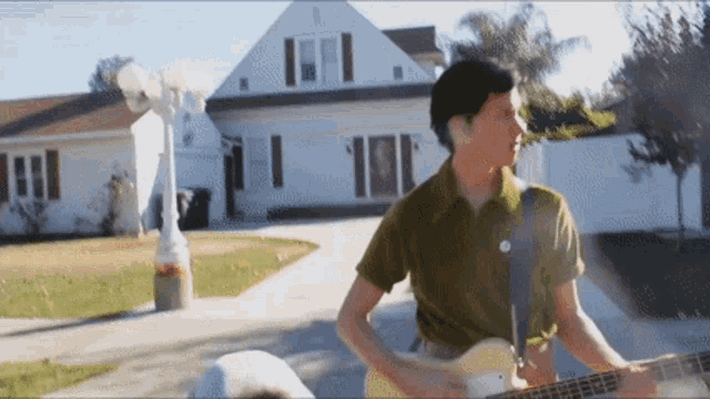 a man in a green shirt is playing a guitar in front of a white house