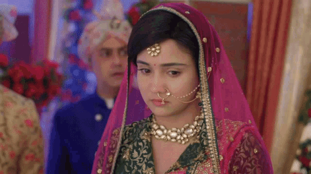 a woman in a pink and green dress with a nose ring is standing in front of a man in a turban .