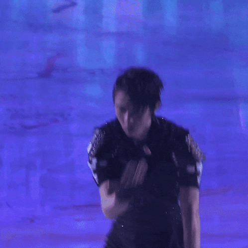 a man in a black outfit is dancing in front of a blue wall