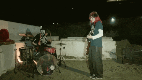 a man in a skeleton mask is playing drums while a woman plays guitar