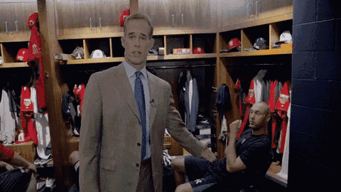 a man in a suit and tie stands in a locker room talking to a baseball player
