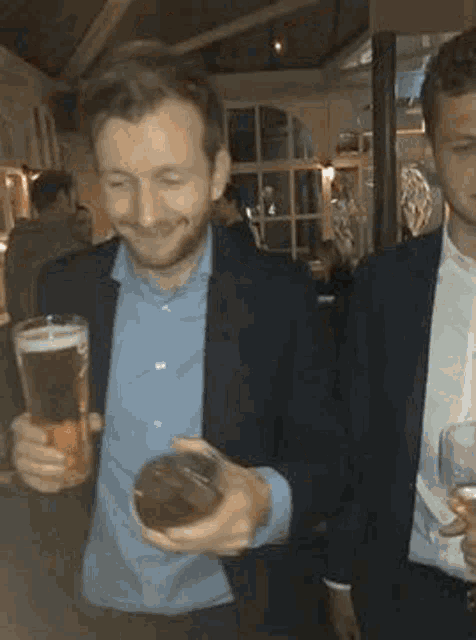 a man in a suit is holding a glass of beer while standing next to another man .