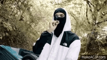 a man wearing a balaclava is smoking a cigarette while standing next to a car .
