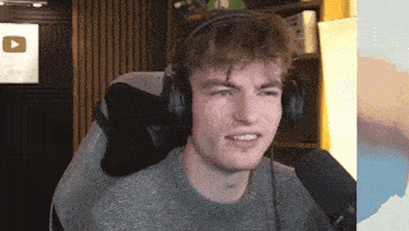 a man wearing headphones and a sweater is sitting in front of a microphone .