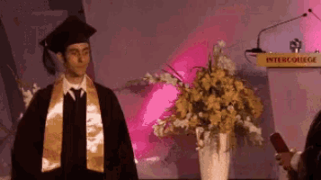 a man in a graduation cap and gown stands in front of a podium that says " inter college "
