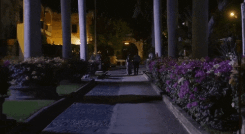 a couple walking down a path with purple flowers