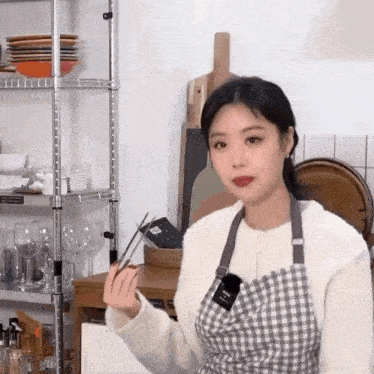 a woman in an apron is holding a pair of chopsticks in her hand .