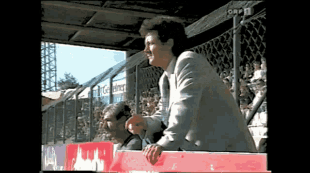 a man in a suit stands in front of a fence that says orf 1