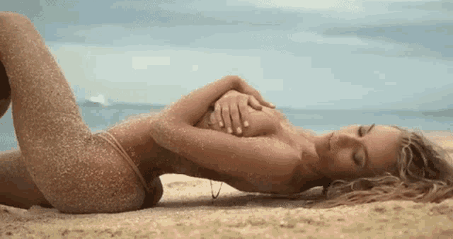 a naked woman in a bikini is laying on a sandy beach .
