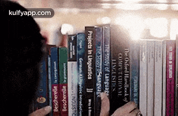 a person is putting books on a shelf and one of the books is titled the story of language