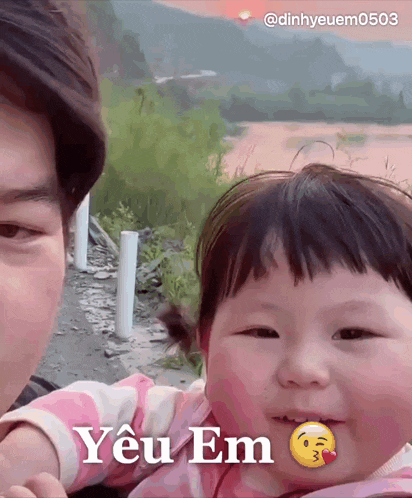 a little girl with a smiley face on her face is being held by a man who says " yêu em "
